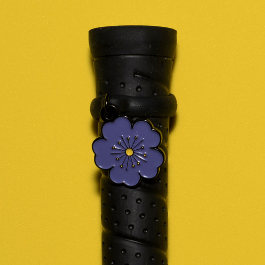 A close-up of a pinsnickety purple Poppy crop charm on a whip handle in front of a yellow background