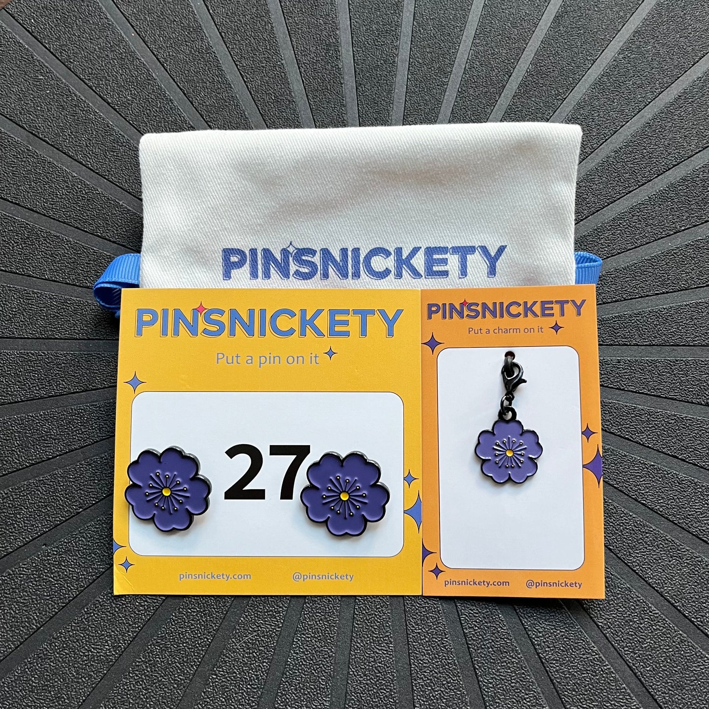 pinsnickety purple poppy matching set, featuring a pair of purple poppy horse show number pins, a purple poppy bridle charm and a pinsnickety twill bag, all displayed on a black background