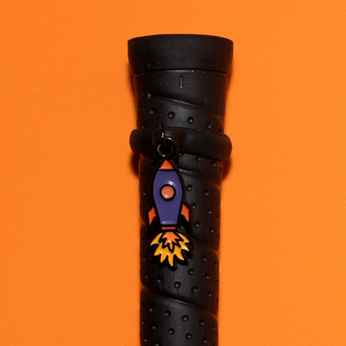 Pinsnickety Rocket Ship crop charm on a whip handle in front of a colored background