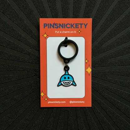 pinsnickety blue and white shark crop charm on an orange product packagine card in front of a textured black background