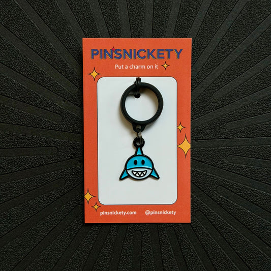 pinsnickety blue and white shark crop charm on an orange product packagine card in front of a textured black background