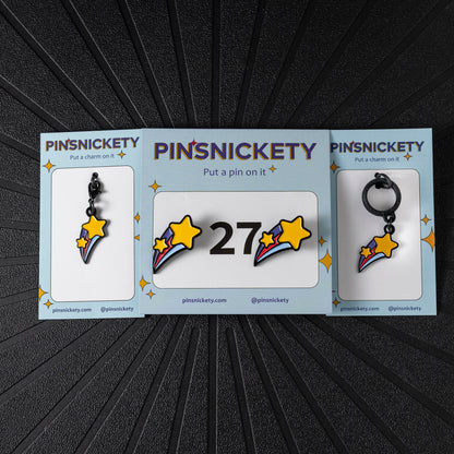A matching triple combination set with Pinsnickety Shooting Star horse show number pins, a bridle charm, and a crop charm in their product packaging on a black background.