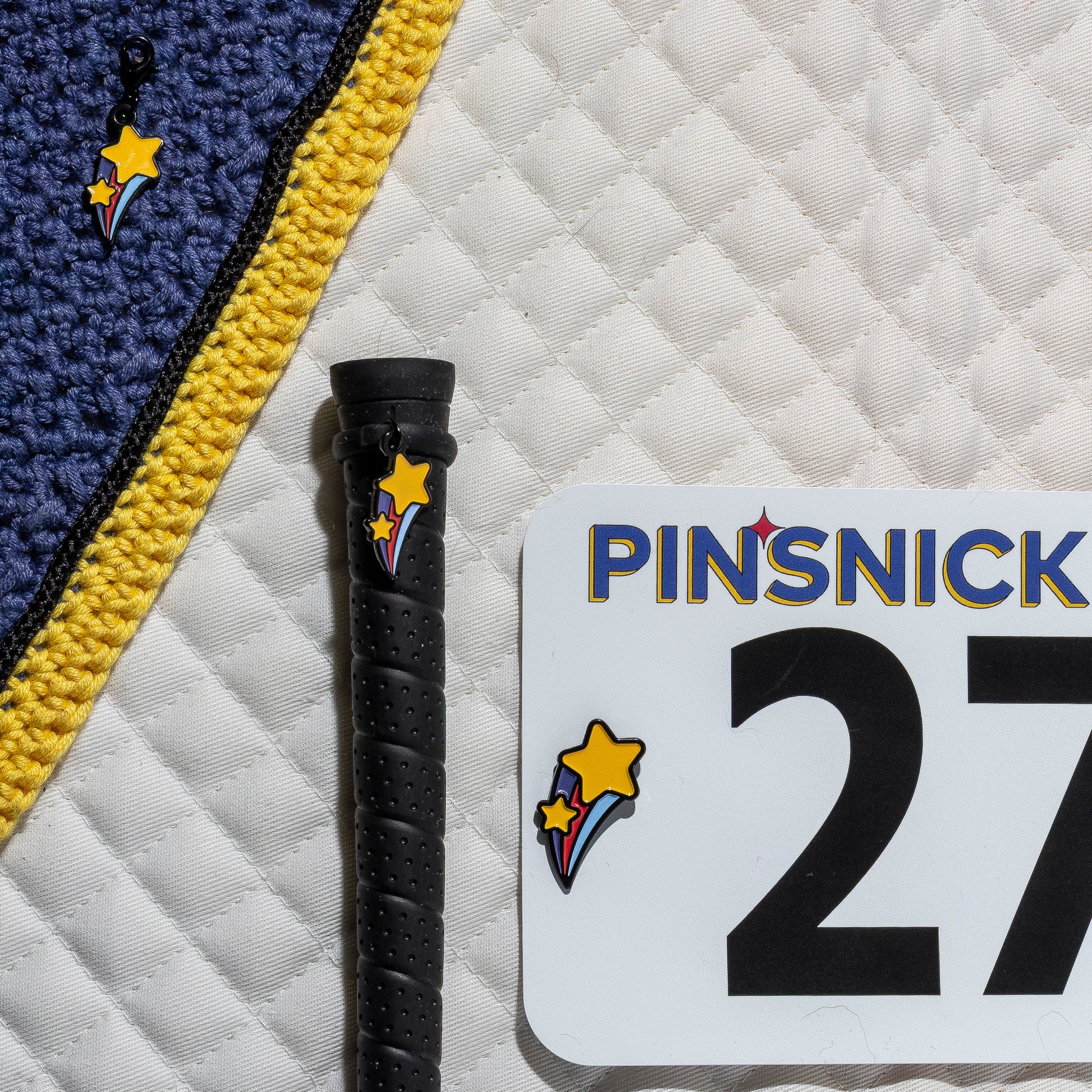 A saddle pad, bonnet and whip decorated with matching Shooting Star Pinsnickety horse show number pins, a bridle charm and a crop charm.