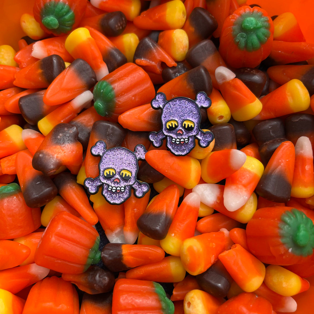 a pair of purple glittery pinsnickety skull-shaped horse show number pins are nestled in a bucket of orange, yellow, white, and brown striped candy corn.