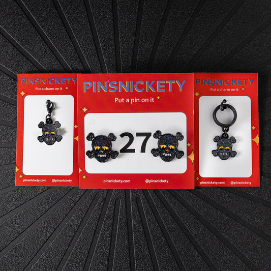 A matching triple combination set with Pinsnickety Skull horse show number pins, a bridle charm, and a crop charm in their product packaging on a black background.