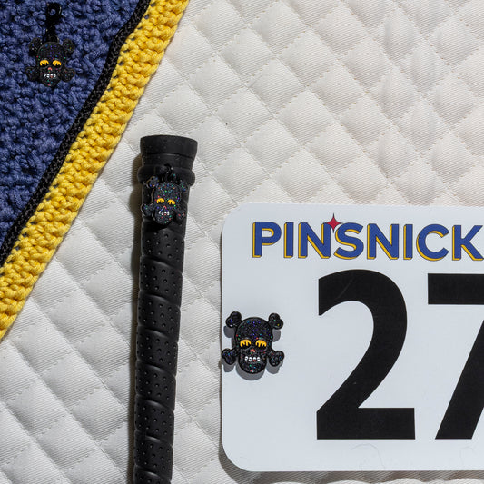 A saddle pad, bonnet and whip decorated with matching Skull Pinsnickety horse show number pins, a bridle charm and a crop charm.