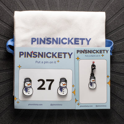 pinsnickety snowman set, featuring a snowman horse show number pin, a snowman bridle charm and a Pinsnickety twill storage bag, on a black background
