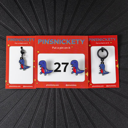 A matching triple combination set with Pinsnickety T-Rex horse show number pins, a bridle charm, and a crop charm in their product packaging on a black background.