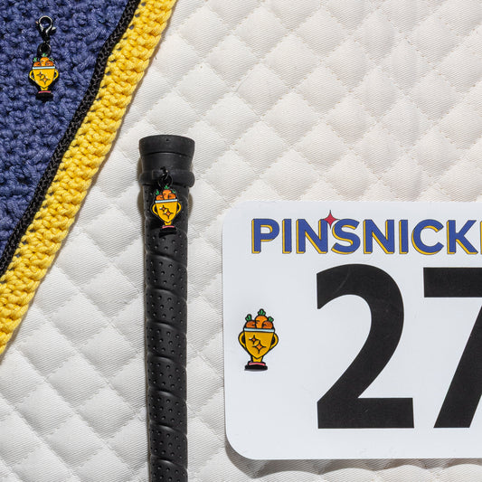 A saddle pad, bonnet and whip decorated with matching Trophy Pinsnickety horse show number pins, a bridle charm and a crop charm.