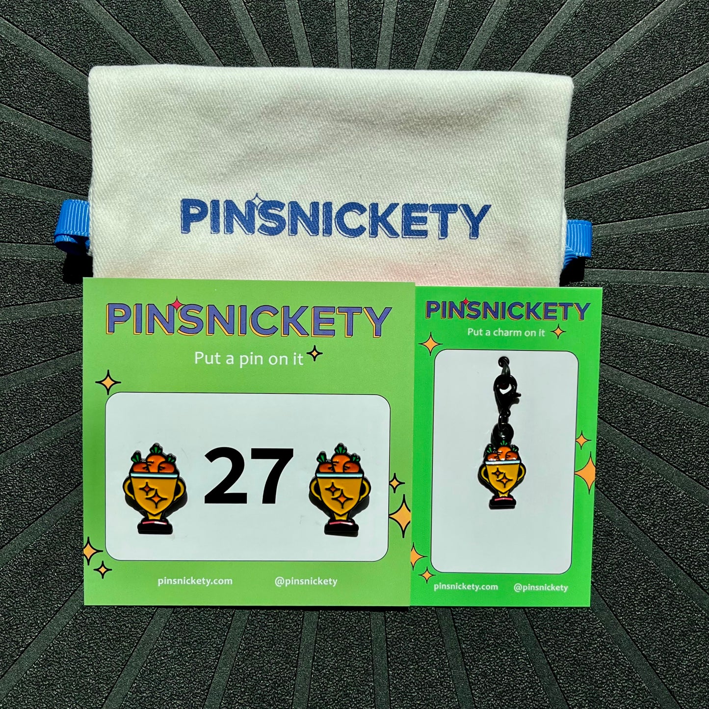 Pinsnickety trophy matching set featuring a pair of trophy horse show number pins, a trophy bridle charm, and a pinsnickety twill storage bag, all on a black background