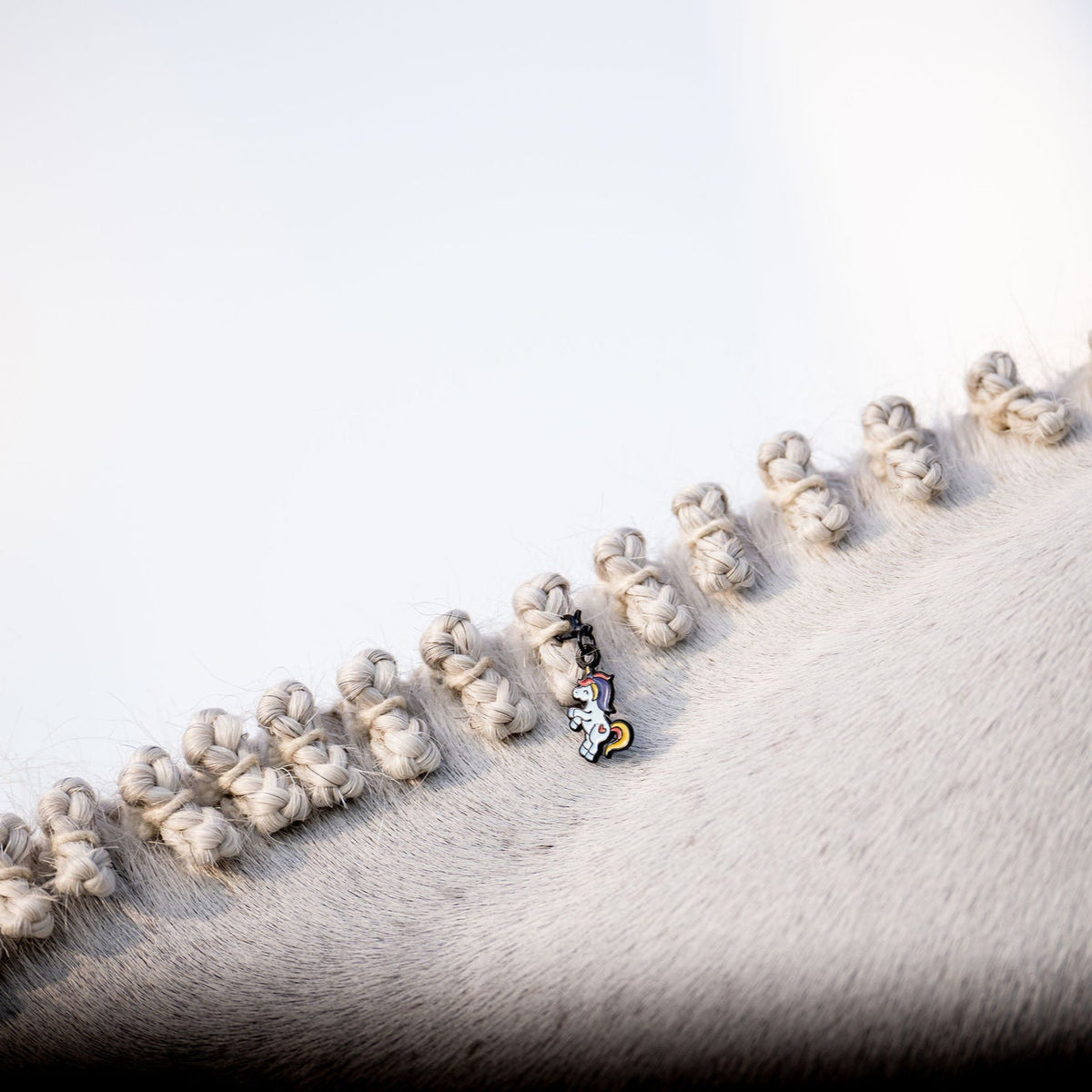 close up of a pinsnickety unicorn bonnet charm on a grey horses's hunter braids