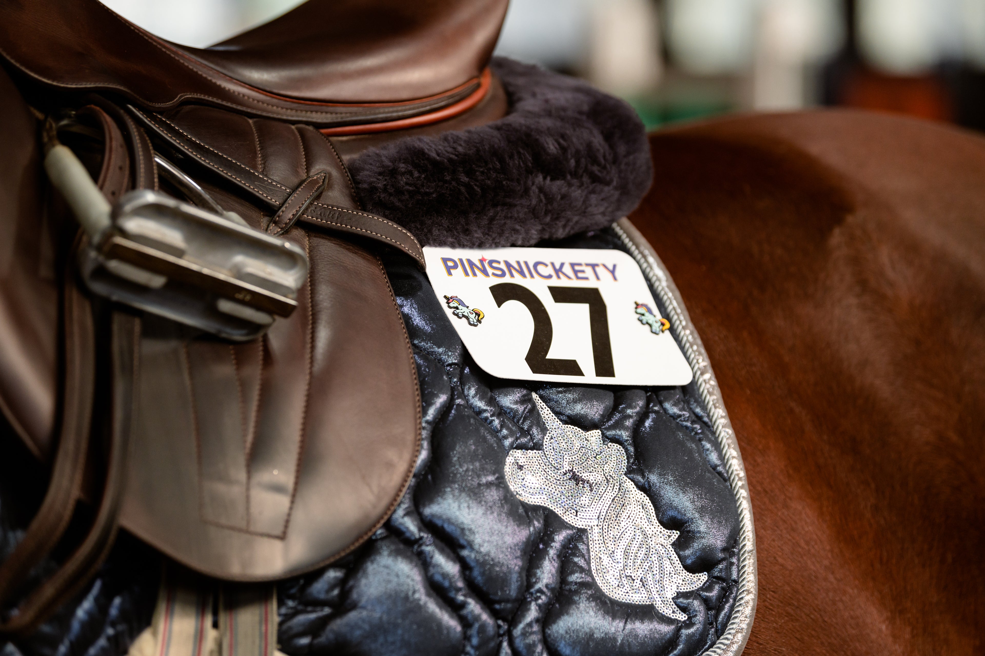 pinsnickety flying unicorn horse show number pins on a blue saddle pad worn by a chestnut horse
