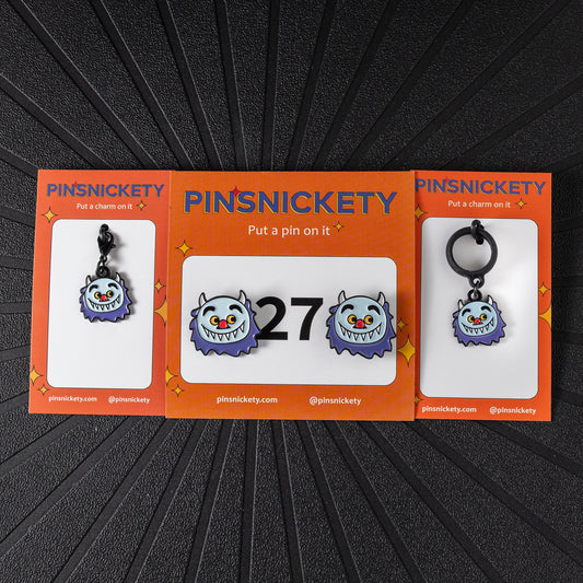 A matching triple combination set with Pinsnickety Wild Thing horse show number pins, a bridle charm, and a crop charm in their product packaging on a black background.