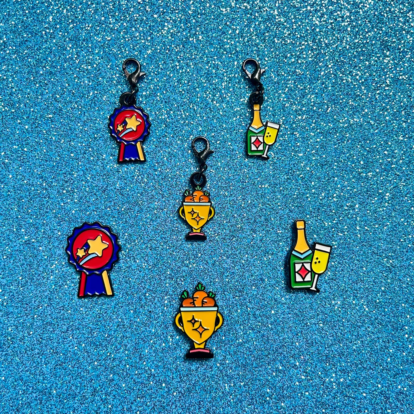 pinsnickety champion, trophy, and champagne horse show number pins and bridle charms against a blue glitter background