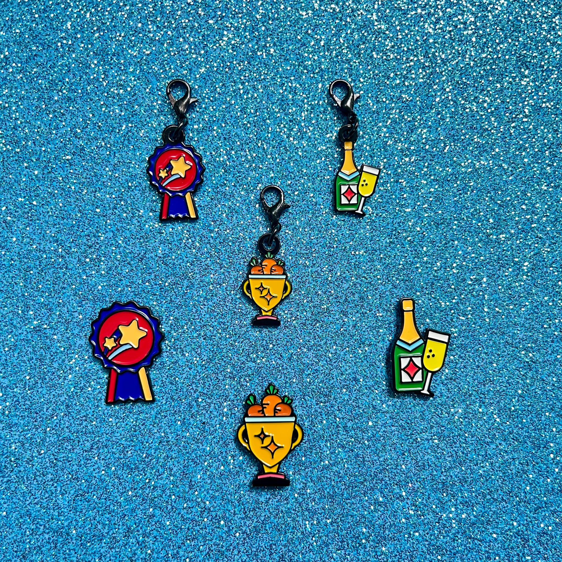 pinsnickety champion, trophy, and champagne horse show number pins and bridle charms against a blue glitter background