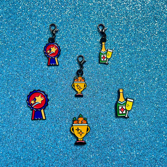 pinsnickety champion, trophy, and champagne horse show number pins and bridle charms against a blue glitter background