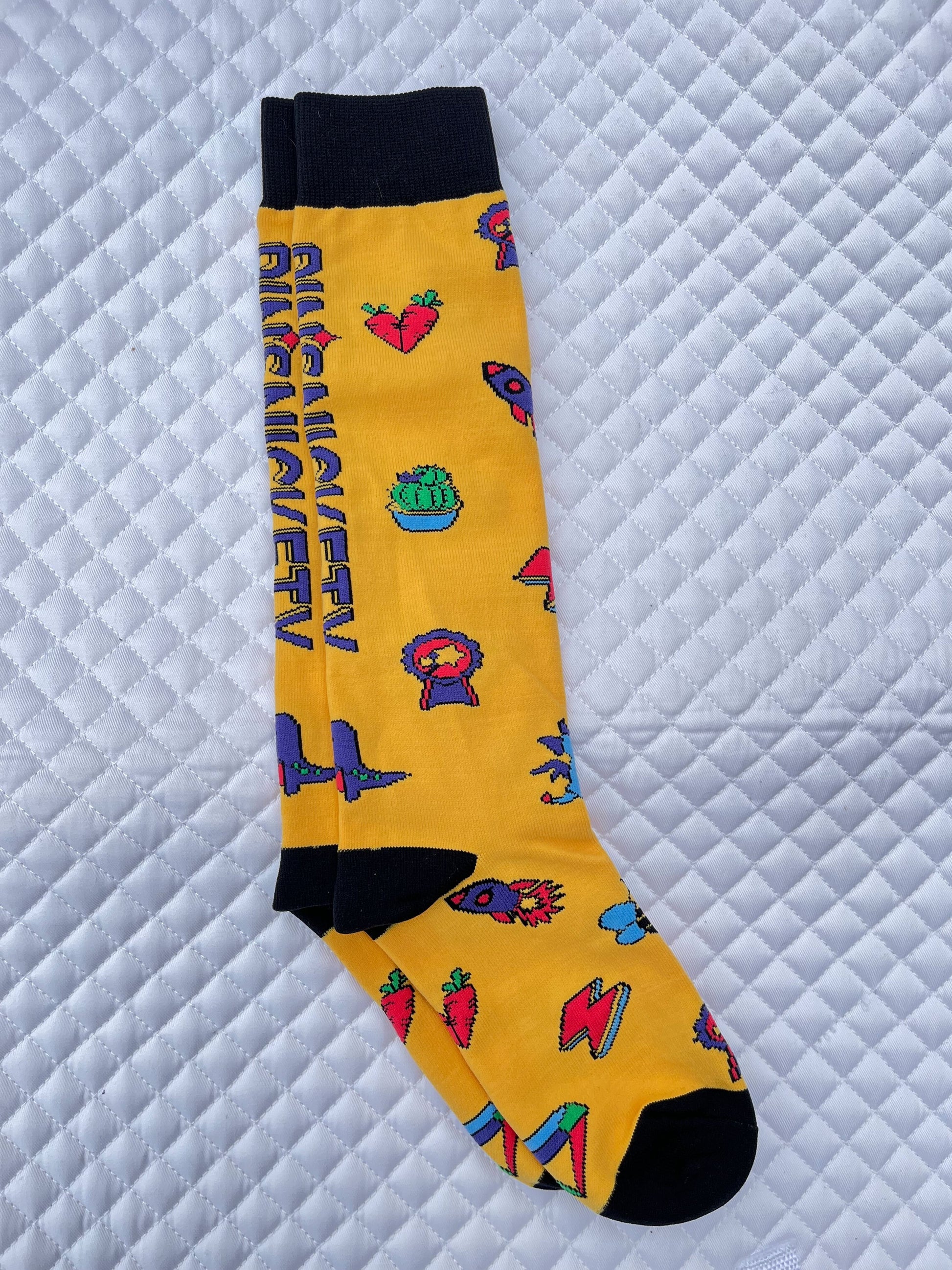 pinsnickety tall boots socks in sunny yellow, covered with pin designs and the company logo, from the right, on a saddle pad 