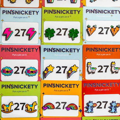 Many of Pinsnickety's horse show number pin designs displayed in a grid on their product packaging cards. Includes newer Lightning Bolt, Clover, BOOM!, Rainbow, and Dragon pins.