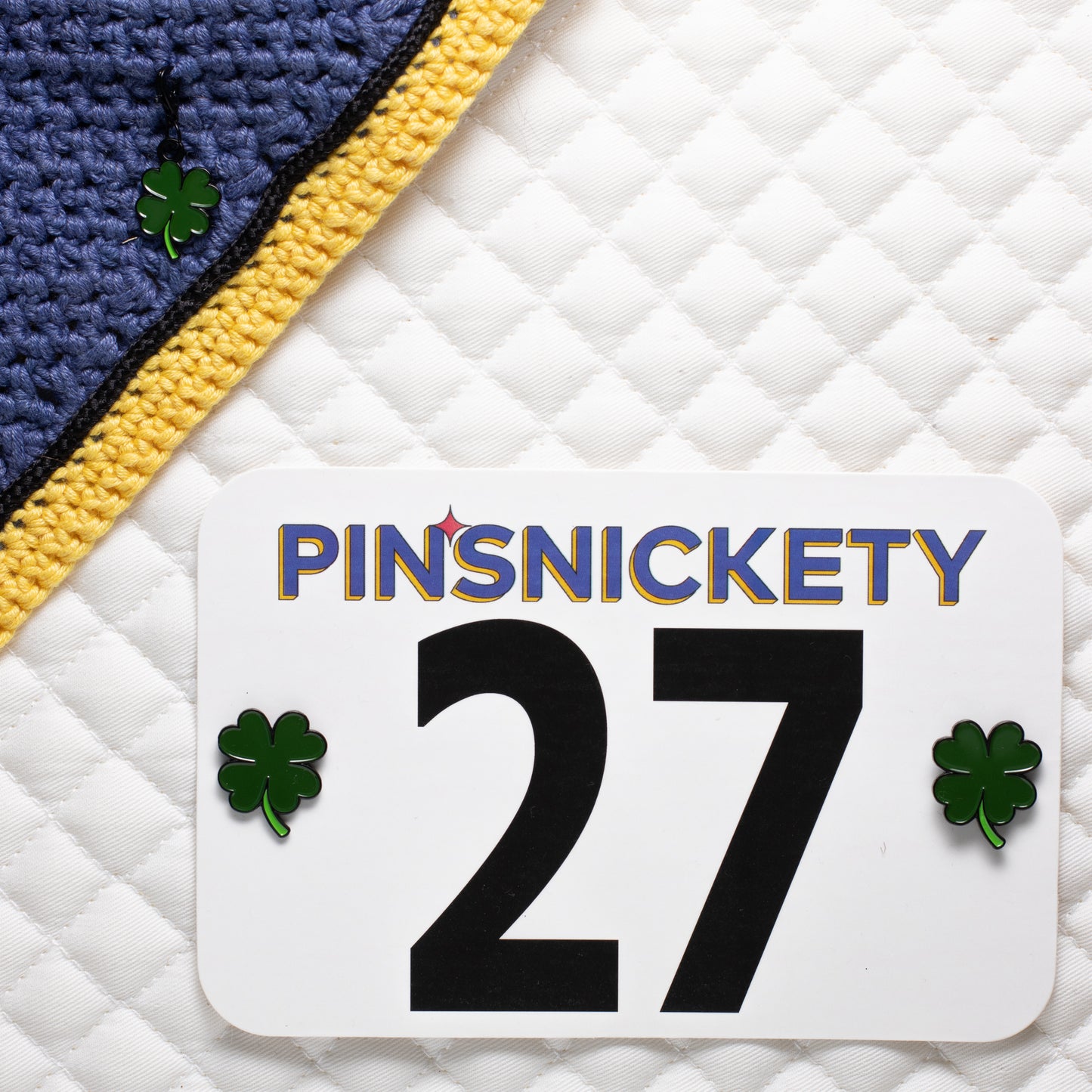pinsnickety clover charm on a bonnet beside clover horse show number pins on a saddle pad