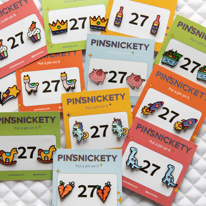 All 12 of Pinsnickety's original horse show number pin designs in their product packaging, displayed on a saddle pad.