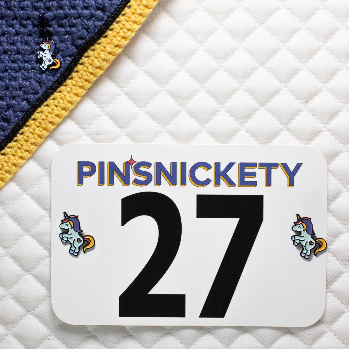 pinsnickety flying unicorn charm on a bonnet and horse show number pins on a saddle pad.